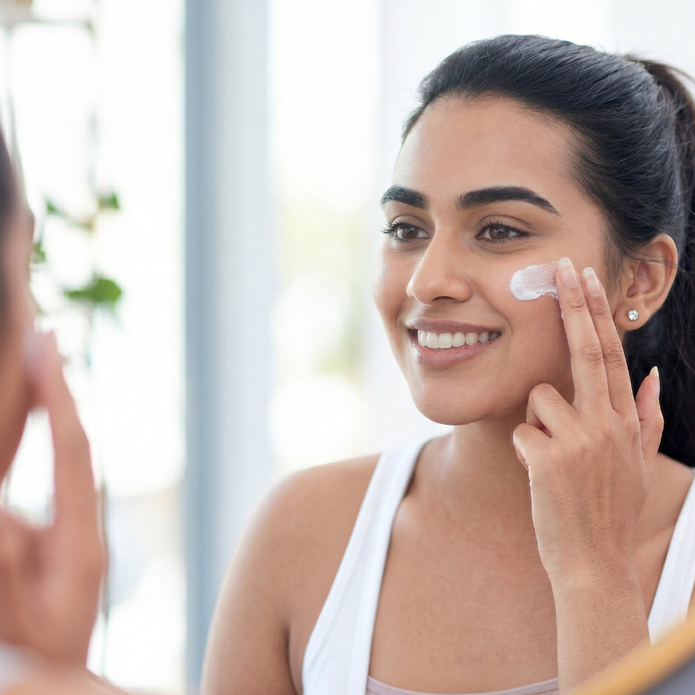 A woman with glowing skin applying cream on her face